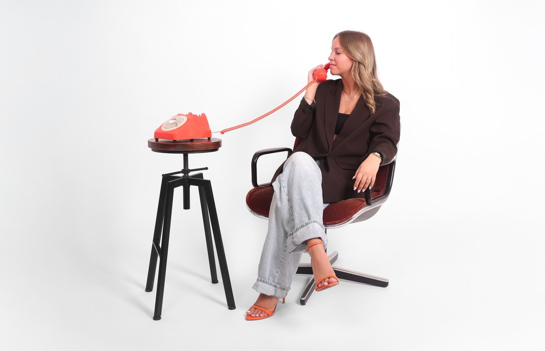 Camille assise dans un fauteuil, téléphone rétro orange à l'oreille
